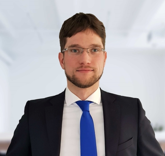A man wearing glasses and a blue tie, looking confidently at the camera.