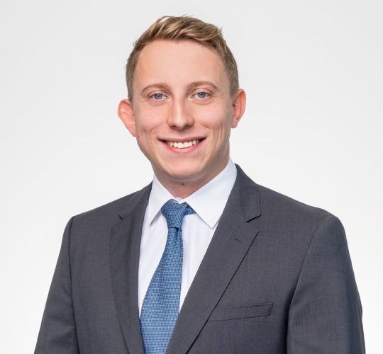 A man in a suit and tie, smiling cheerfully, conveying a professional demeanor.