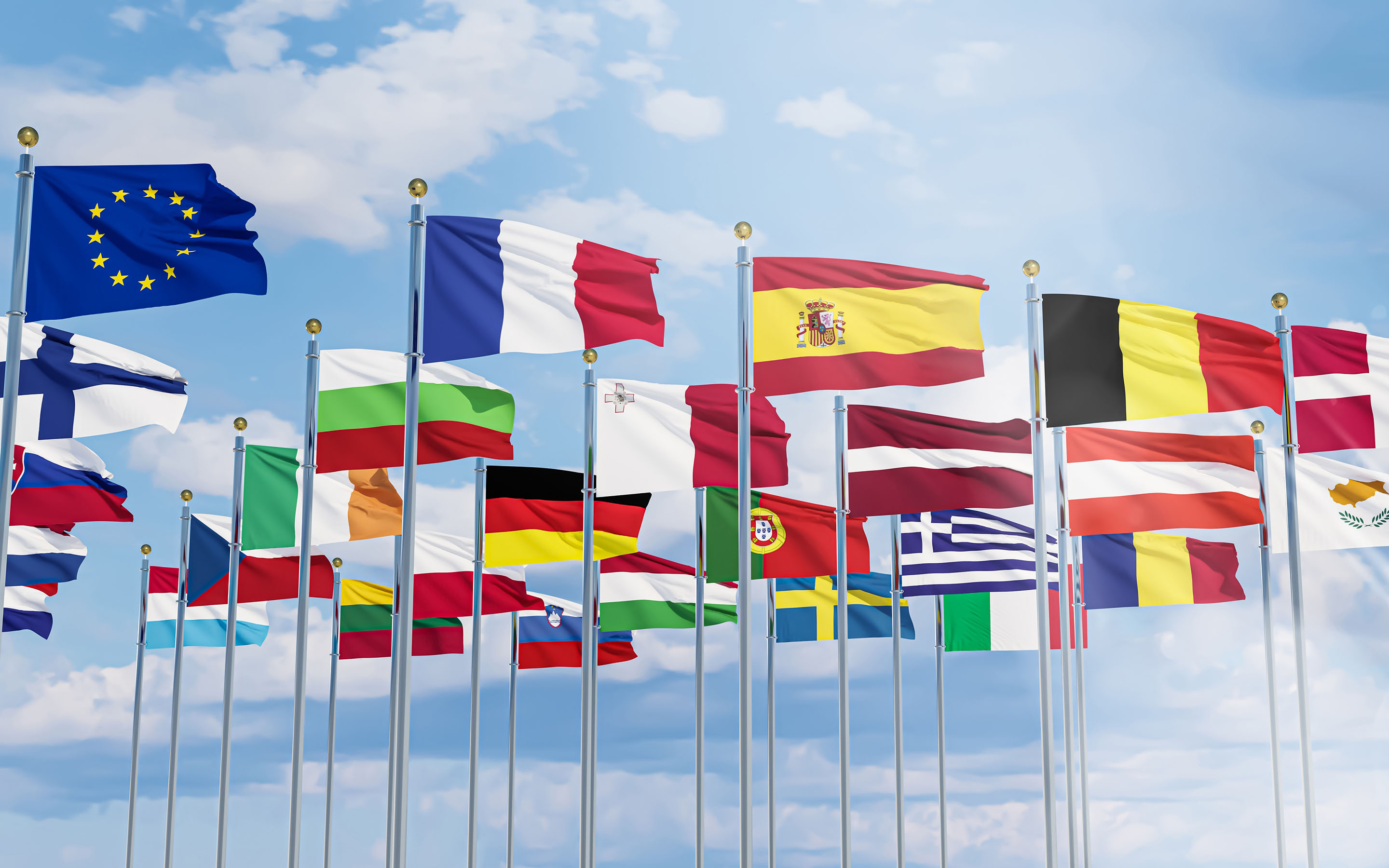 European national flags and the EU flag on flagpoles against a partly cloudy sky.