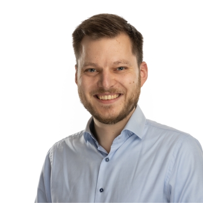 Camiel staat op de foto. Hij draagt een lichtblauw overhemd en glimlacht naar de camera.