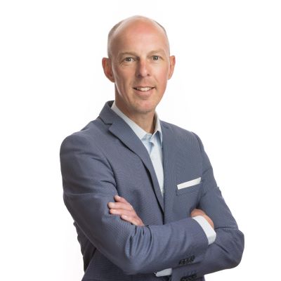 Portretfoto van Dico van Dijk, een professional in zakelijke kleding, die zelfverzekerd glimlacht tegen een neutrale achtergrond.