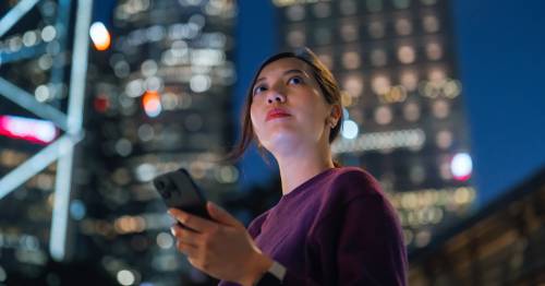 Een vrouw die een smartphone vasthoudt en in de verte kijkt.