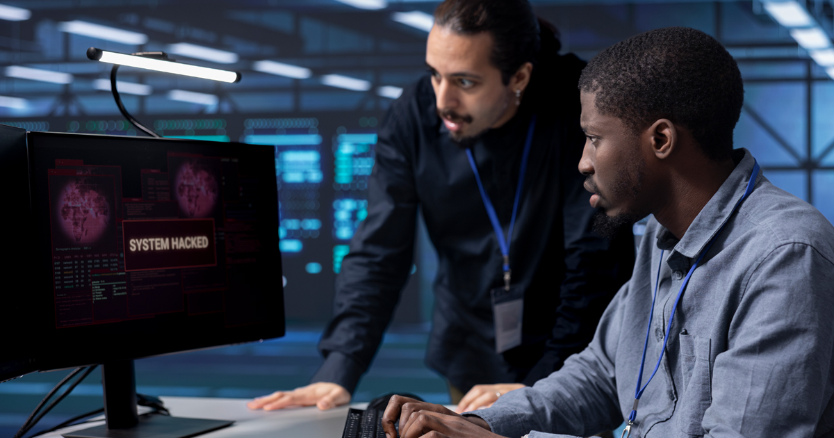 Twee professionals die bezorgd naar een computerscherm kijken waarop een melding staat dat het systeem is gehackt.