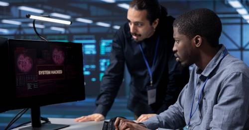 Twee professionals die bezorgd naar een computerscherm kijken waarop een melding staat dat het systeem is gehackt.