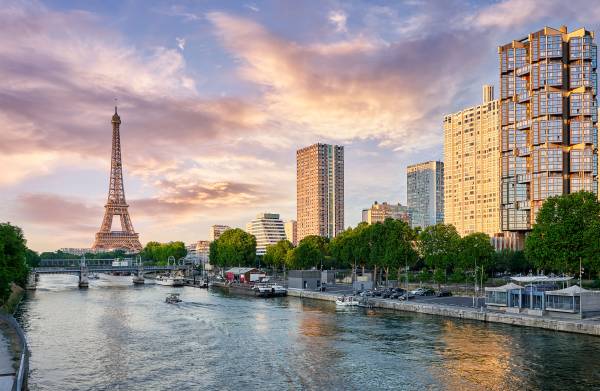 View of the Seine River in Paris with the Eiffel Tower, modern buildings, and boats under a glowing sky.