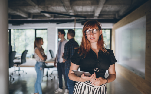 a youn girl in glasses in front of the camera is holding a brochure