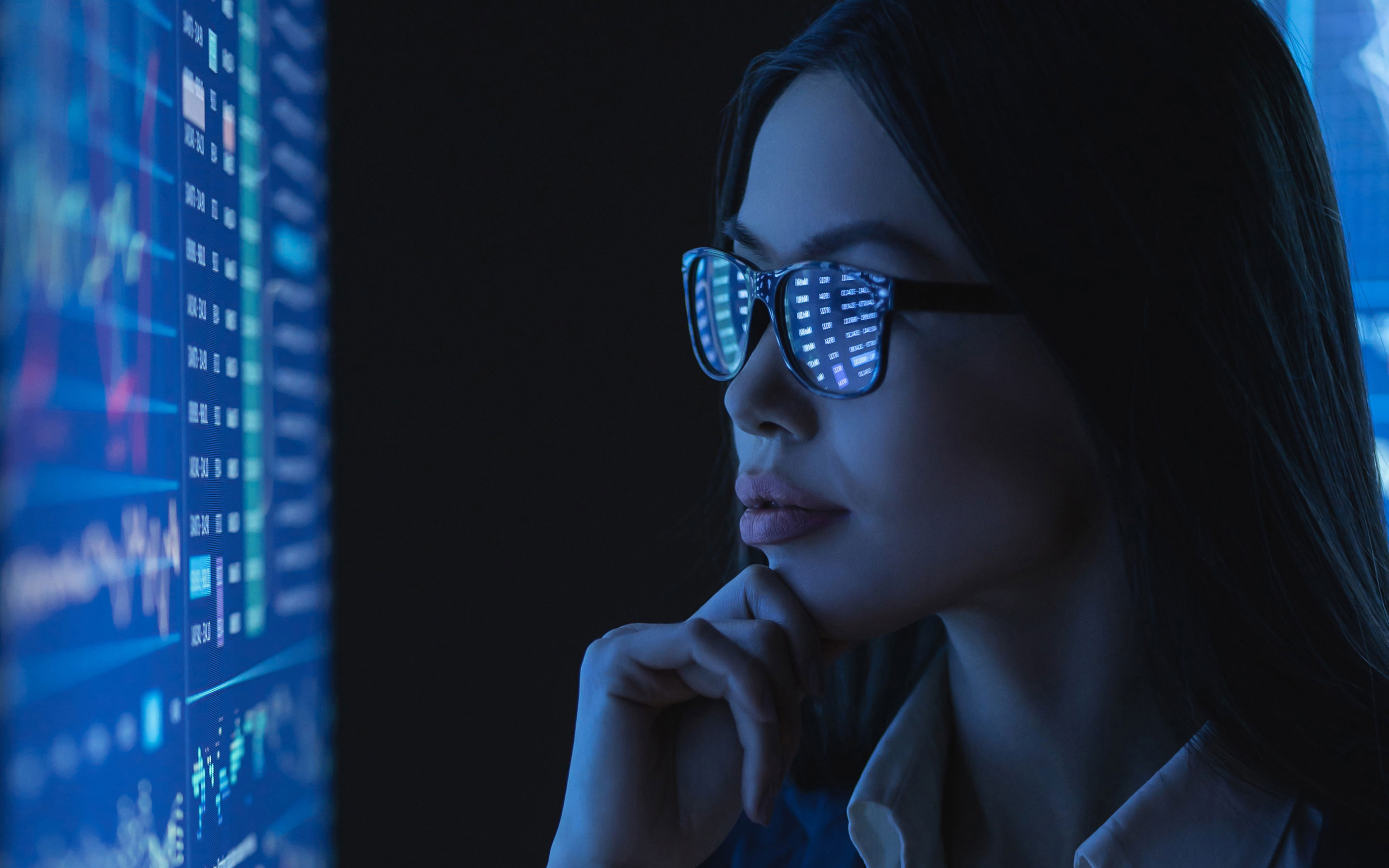 young woman in glasses sitting in the dark in front of the screen