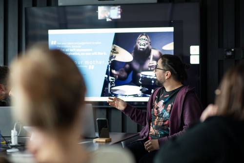 młody mężczyzna w okularach przedstawia na telewizorze w sali konferencyjnej prezentację technologiczną