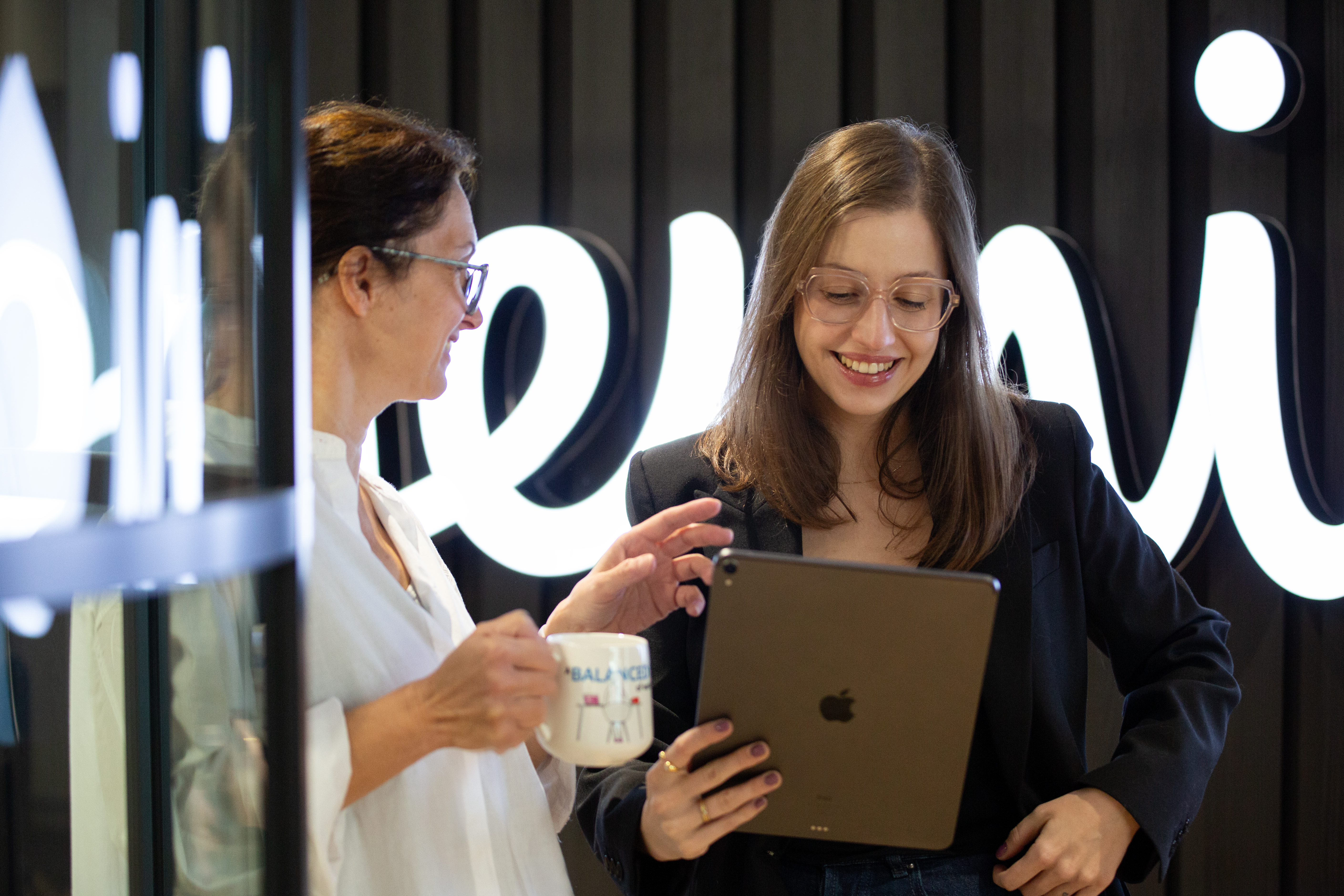 dwie kobiety, jedna trzymająca tablet i słuchająca drugiej