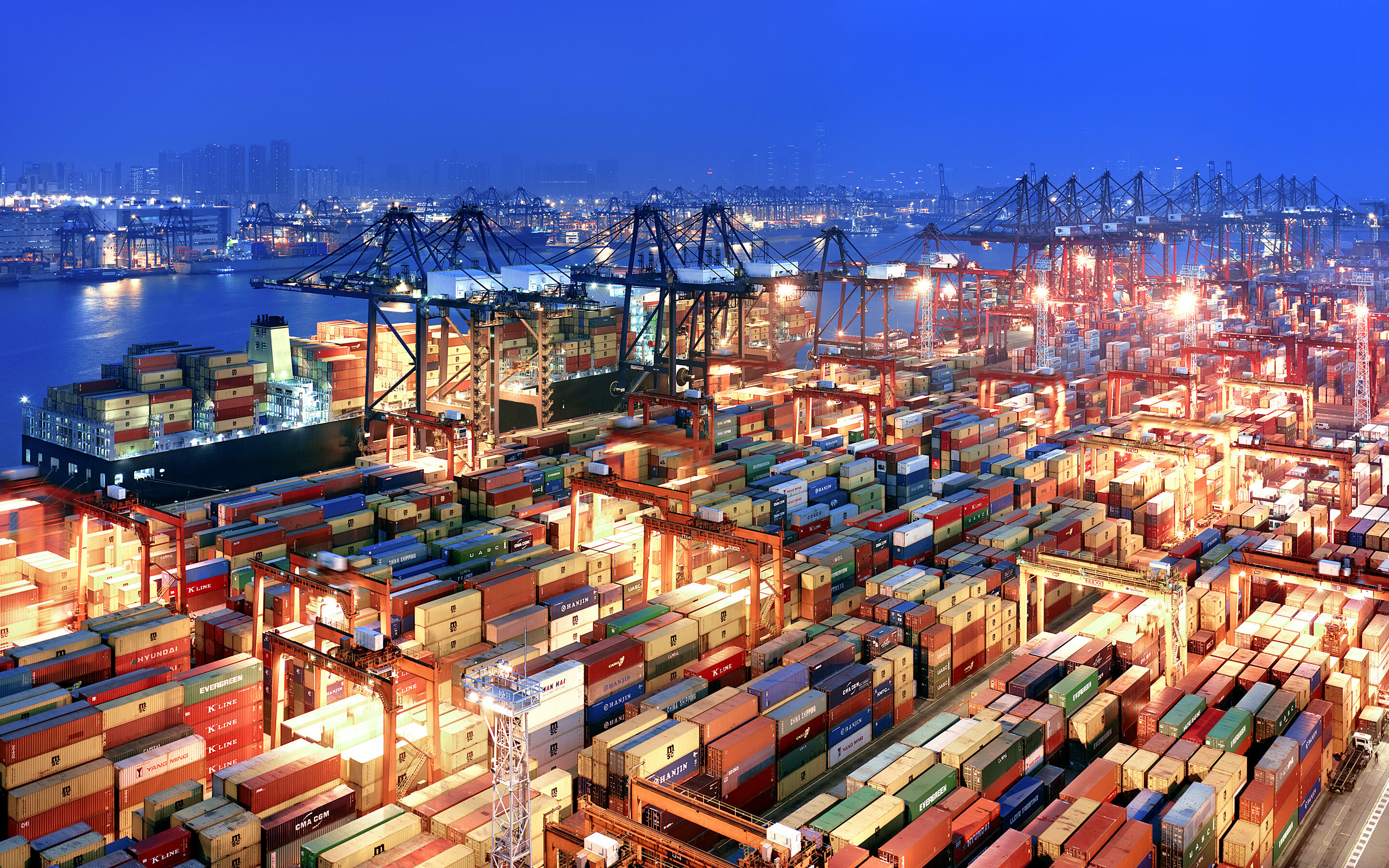 A large container port illuminated at night, filled with numerous shipping containers stacked high
